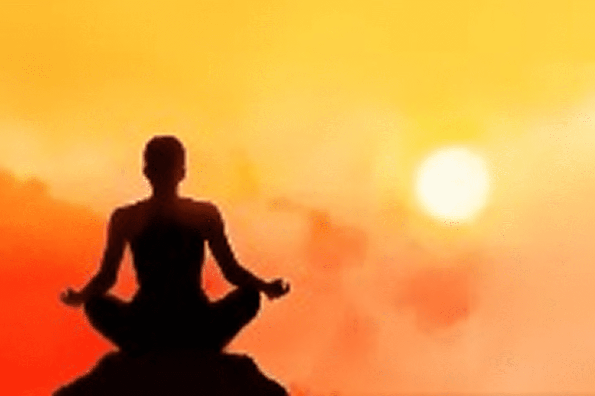 Silhouette meditating at sunset with orange sky.