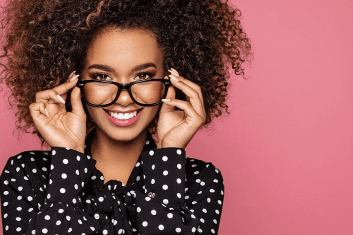 Smiling woman with glasses, pink background.