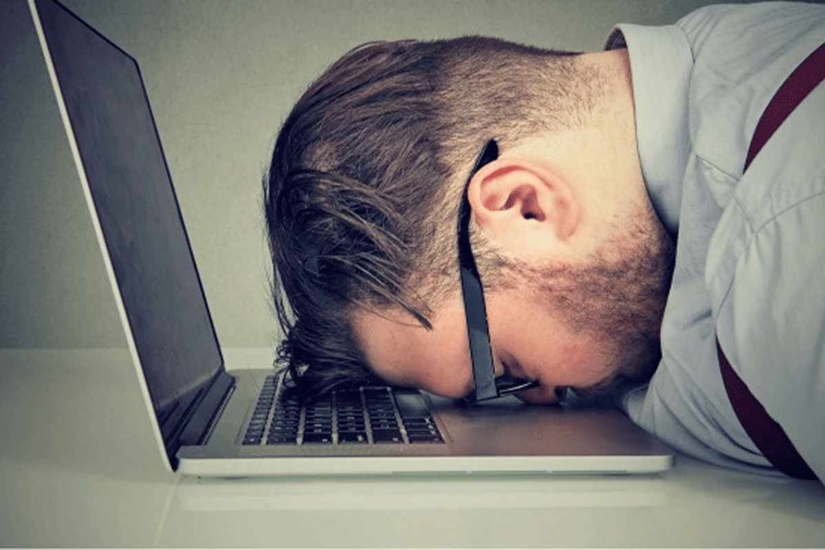 Man asleep on laptop keyboard, looking exhausted.