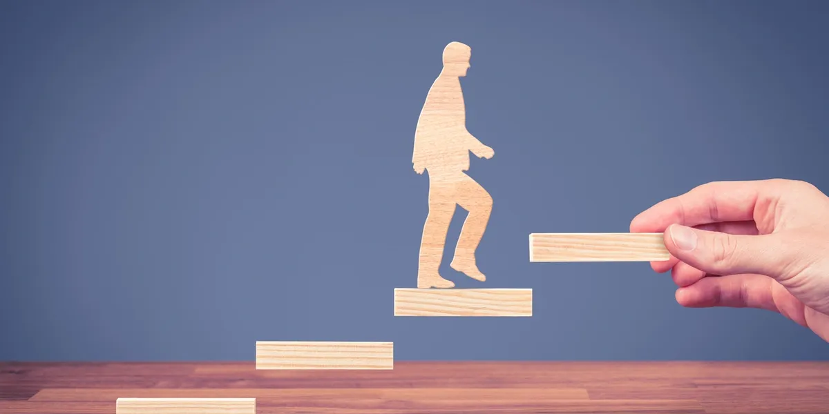 Silhouette of a person climbing wooden steps against a blue sky.